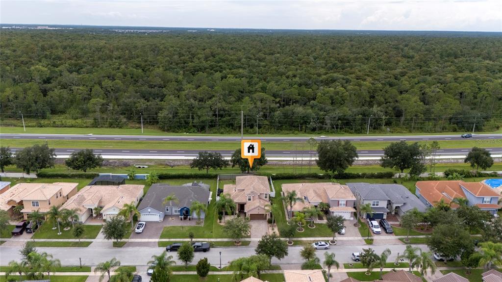 An aerial view shows a suburban neighborhood street with houses backed by a dense forest — 4089 NAVIGATOR WAY, KISSIMMEE, FL