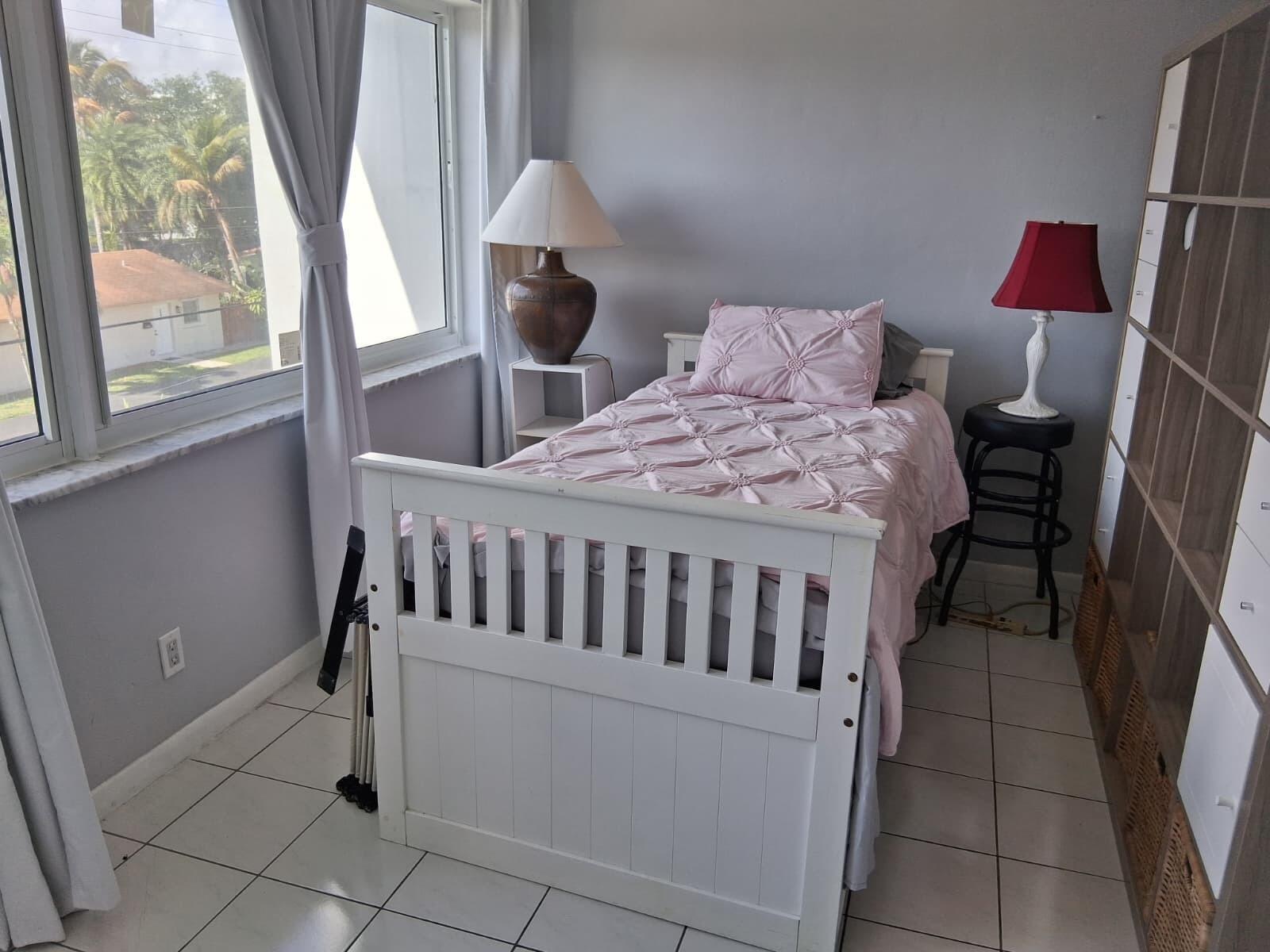 A bedroom features a white bed frame, a pink quilted comforter, and a tall shelving unit — 329 SE 3rd Street # 302s, Hallandale Beach FL 33009, HALLANDALE BEACH, FL