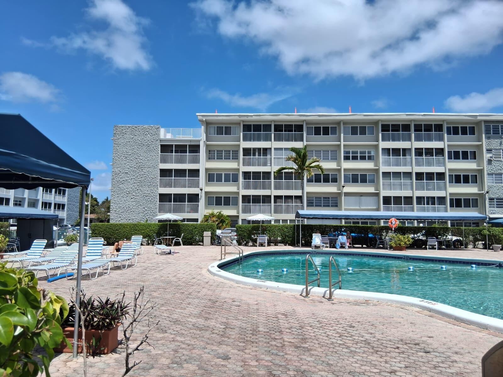 A swimming pool with lounge chairs sits in front of a multi-story apartment building — 329 SE 3rd Street # 302s, Hallandale Beach FL 33009, HALLANDALE BEACH, FL