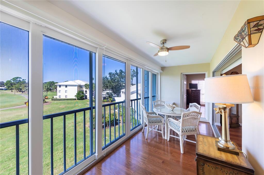 A sunroom features wood flooring, a ceiling fan, wicker furniture, and views of a golf course — 437 CERROMAR LANE UNIT 525, VENICE, FL