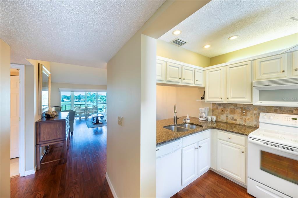 A kitchen with white cabinets and granite countertops opens into a living area with balcony — 437 CERROMAR LANE UNIT 525, VENICE, FL