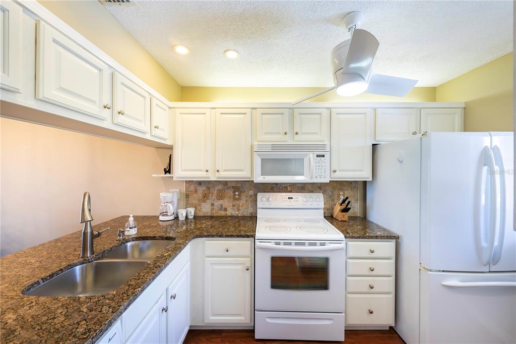 A kitchen with white cabinets, granite countertops, a white stove, and a white refrigerator — 437 CERROMAR LANE UNIT 525, VENICE, FL