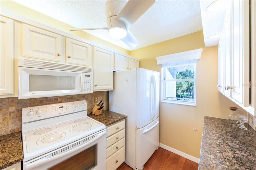 A galley kitchen features white cabinets, granite countertops, a white stove, and a white refrigerator — 437 CERROMAR LANE UNIT 525, VENICE, FL
