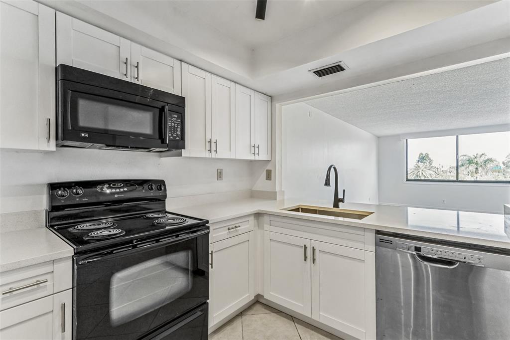 A kitchen features white cabinets, black appliances, a stainless steel dishwasher, and a sink — 6219 PALMA DEL MAR BOULEVARD S UNIT 301, ST PETERSBURG, FL