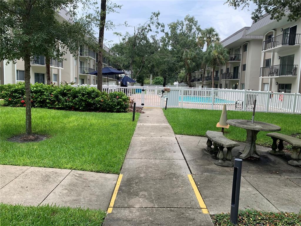 A concrete walkway leads to a fenced swimming pool area between two apartment buildings — 4611 W FIG STREET UNIT 210, TAMPA, FL