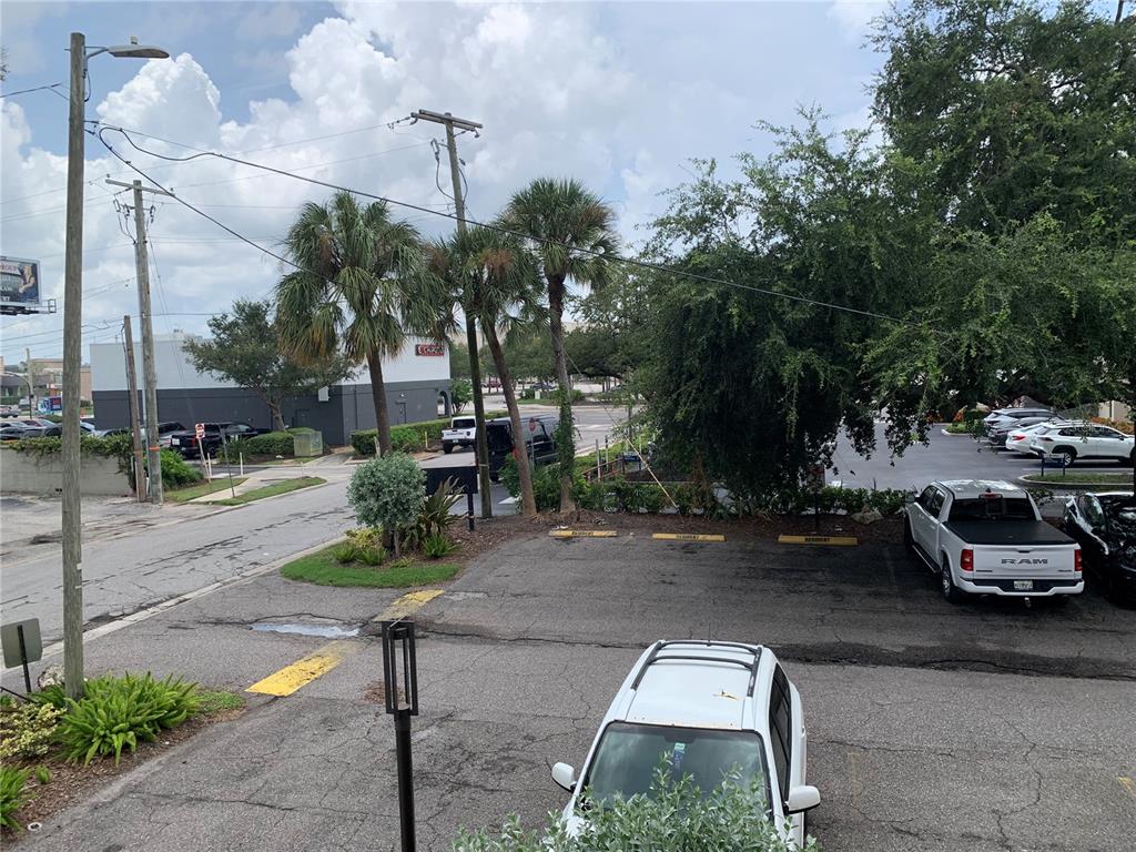 An elevated view of a parking lot with several vehicles, palm trees, and a building — 4611 W FIG STREET UNIT 210, TAMPA, FL