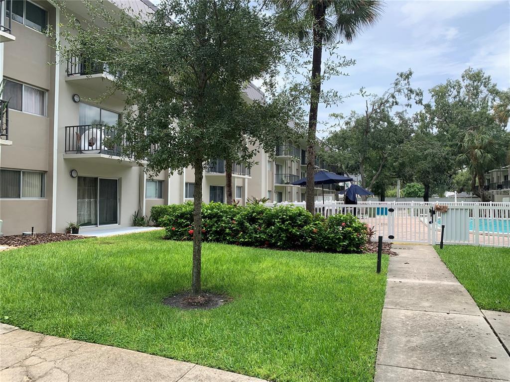 A multi-story apartment building exterior with a lawn, trees, and a fenced pool area — 4611 W FIG STREET UNIT 210, TAMPA, FL