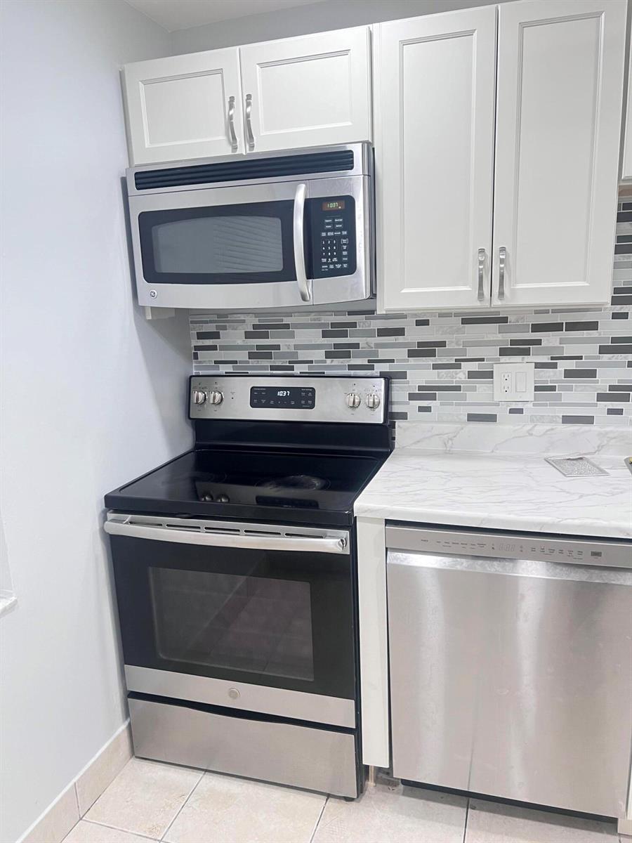 A kitchen features stainless steel appliances, white cabinets, and a gray and white tiled backsplash — 7505 NW 5th Place # 106, Margate FL 33063, MARGATE, FL