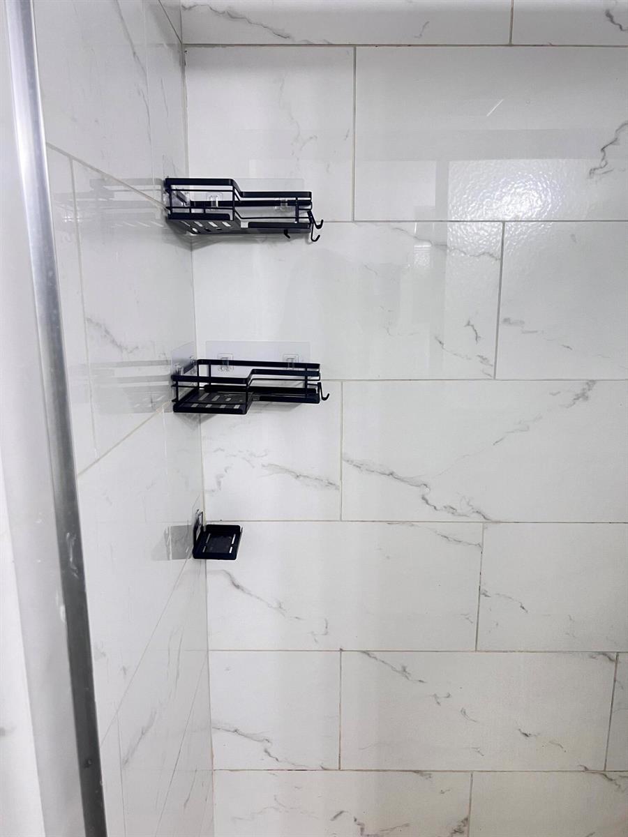 A shower stall features white marble-look wall tiles and three black metal storage shelves — 7505 NW 5th Place # 106, Margate FL 33063, MARGATE, FL
