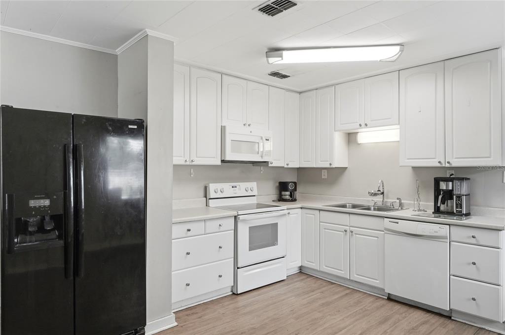 A kitchen features white cabinets, a black refrigerator, a white stove, and light wood flooring — 730 WESTOVER PARKWAY, BARTOW, FL