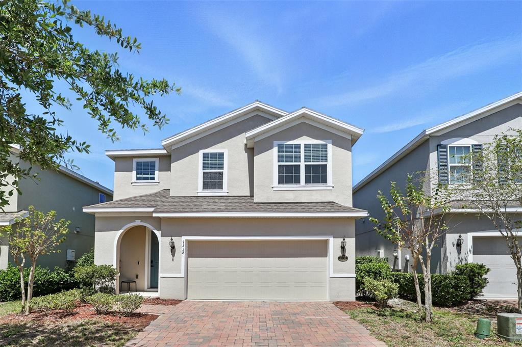 A two-story suburban house with a beige stucco exterior, a two-car garage, and a paver driveway — 1338 RILEY CIRCLE, DELAND, FL