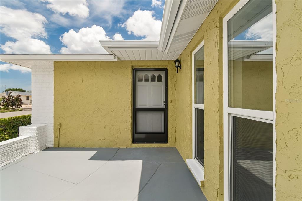 A yellow stucco exterior wall features a front door with a screen and two windows — 11130 TAMARIX AVE, PORT RICHEY, FL