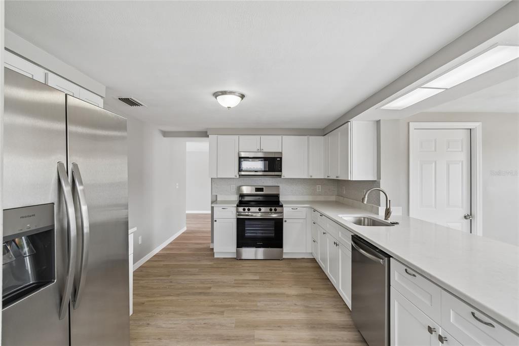A kitchen with white cabinets, stainless steel appliances, and light wood-look flooring — 11130 TAMARIX AVE, PORT RICHEY, FL