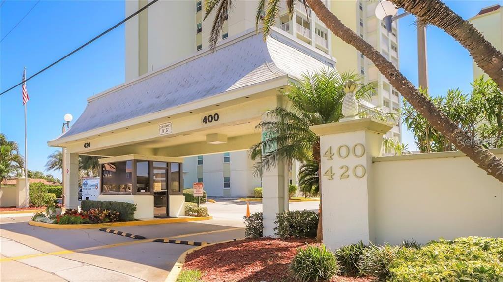 The exterior view shows a gated entrance with a security booth and building numbers — 400 64TH AVENUE UNIT 1001 W, ST PETE BEACH, FL