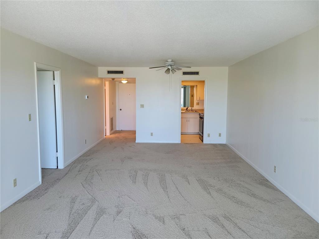 An empty living room with beige carpet, a ceiling fan, and a view into a kitchen — 400 64TH AVENUE UNIT 1001 W, ST PETE BEACH, FL