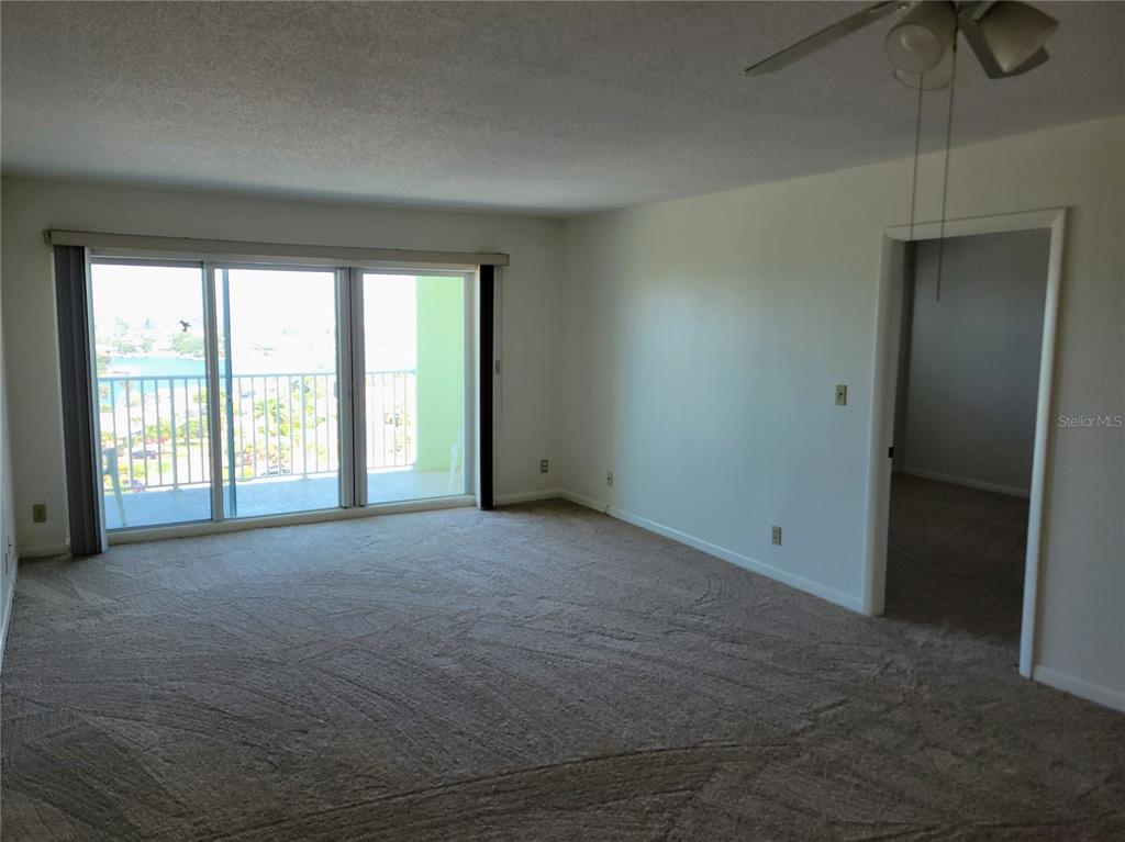 A carpeted living room features a large sliding glass door leading to a balcony — 400 64TH AVENUE UNIT 1001 W, ST PETE BEACH, FL