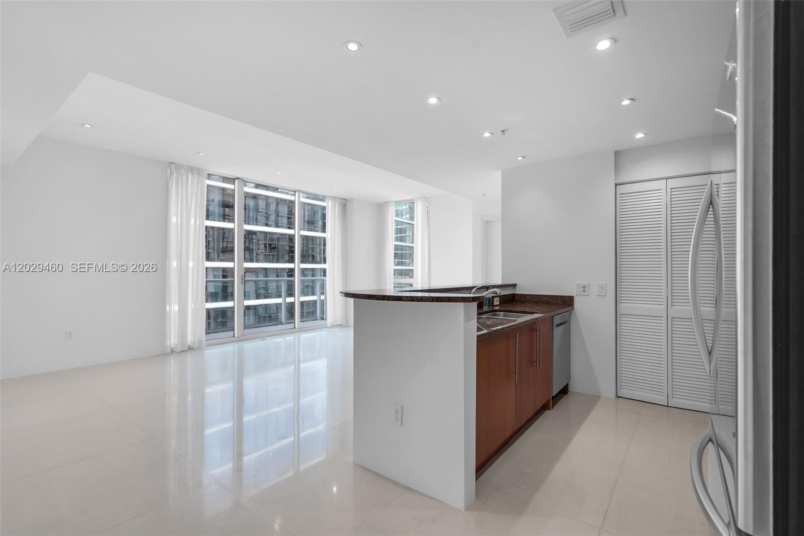 A kitchen with wood cabinets and granite countertops overlooks a bright, open living area — 300 S Biscayne Blvd # 3702, Miami FL 33131, MIAMI, FL
