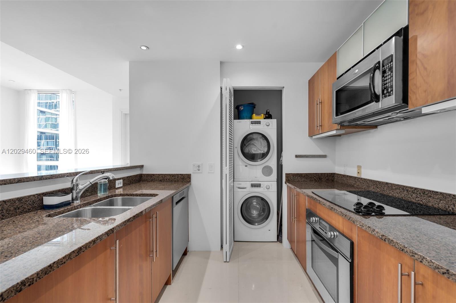 A galley kitchen features wood cabinets, granite countertops, stainless steel appliances, and a stacked laundry unit — 300 S Biscayne Blvd # 3702, Miami FL 33131, MIAMI, FL