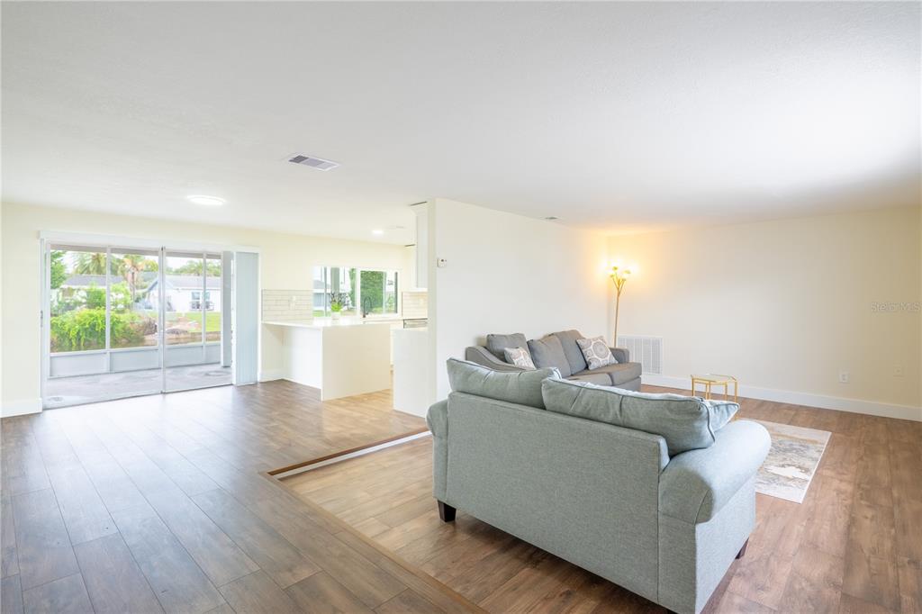 A living room with wood-look flooring features a gray sofa and a sliding glass door — 4016 GRAYTON DRIVE, NEW PORT RICHEY, FL