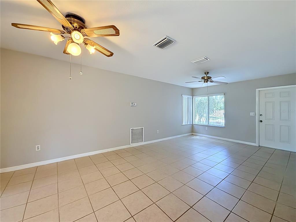 An empty living room features light tile flooring, two ceiling fans, and a white door — 4804 BATCHELOR AVENUE, NORTH PORT, FL