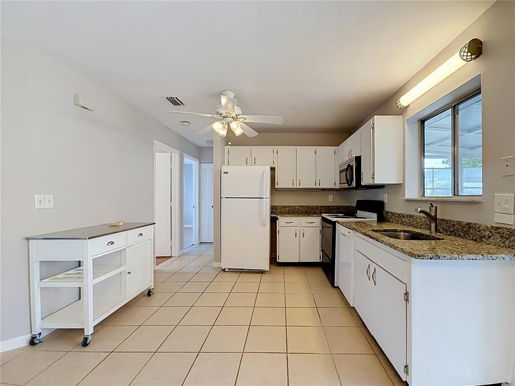 A kitchen with white cabinets, granite countertops, tile flooring, and a white rolling island — 4804 BATCHELOR AVENUE, NORTH PORT, FL