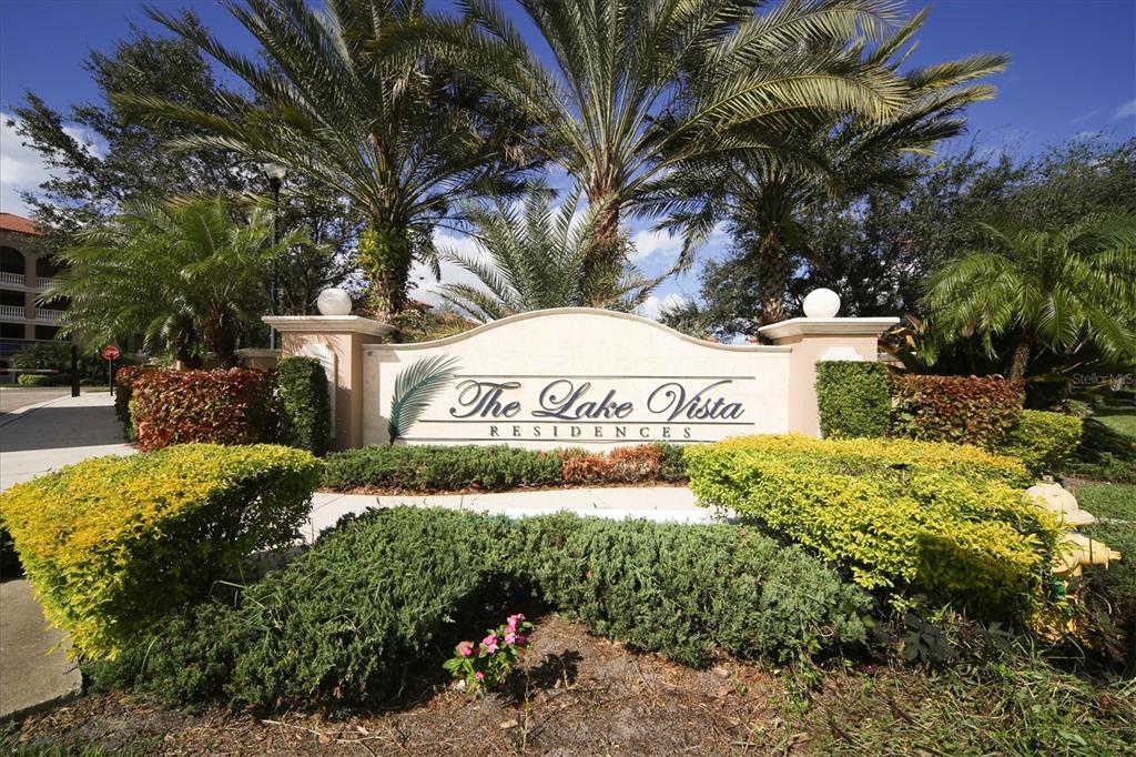A stone monument sign for The Lake Vista Residences sits amidst palm trees and landscaping — 7710 LAKE VISTA COURT UNIT 205, LAKEWOOD RANCH, FL
