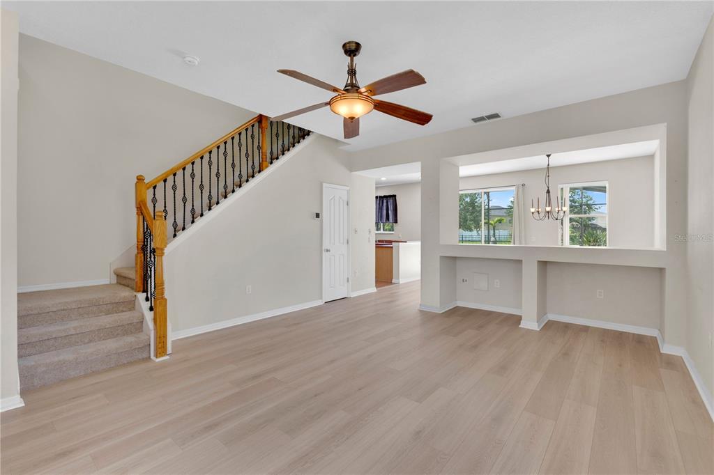 A living room with light wood flooring, a carpeted staircase, and a pass-through wall opening — 3432 PERCHING ROAD, ST CLOUD, FL