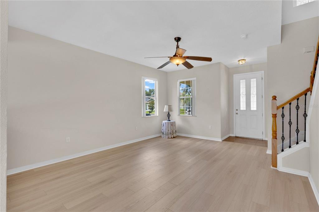 An empty room with light wood flooring, a ceiling fan, and a staircase — 3432 PERCHING ROAD, ST CLOUD, FL