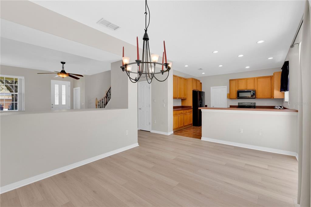 A dining area with light wood flooring, a chandelier, and an adjacent open-concept kitchen — 3432 PERCHING ROAD, ST CLOUD, FL