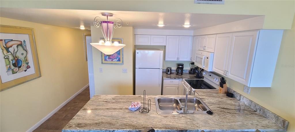 A kitchen features white cabinets, a granite countertop, a double sink, and a refrigerator — 300 N ATLANTIC AVENUE UNIT 1106, DAYTONA BEACH, FL