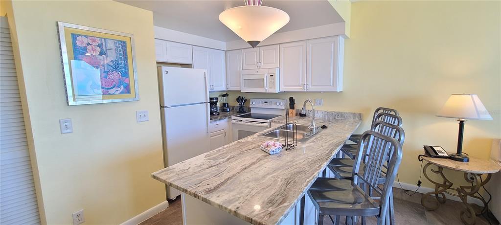 A kitchen features white cabinets, granite countertops, a breakfast bar with stools, and yellow walls — 300 N ATLANTIC AVENUE UNIT 1106, DAYTONA BEACH, FL