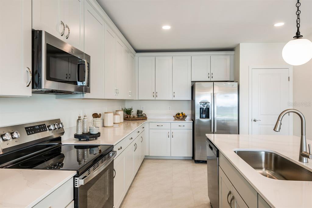 A modern kitchen features white cabinetry, stainless steel appliances, and a central island with sink — 13688 LOREDO WAY, PUNTA GORDA, FL