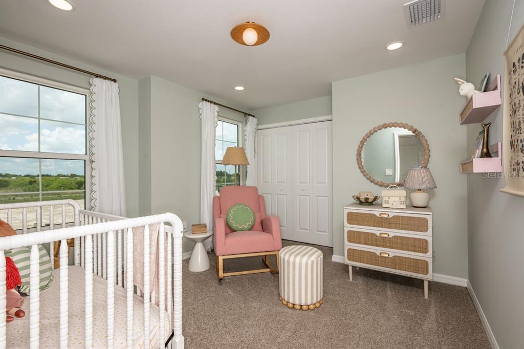 A nursery features a white crib, a pink armchair, a dresser with a mirror, and carpet — 13688 LOREDO WAY, PUNTA GORDA, FL