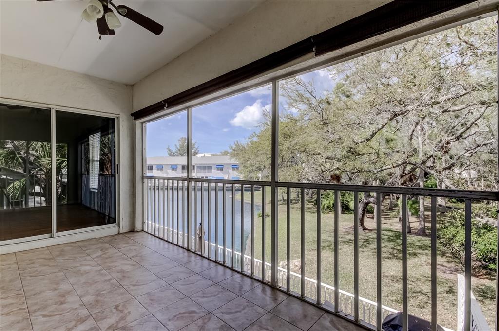 A tiled balcony with a ceiling fan overlooks a canal and trees through screened walls — 11303 SHIPWATCH LANE UNIT 1865, LARGO, FL