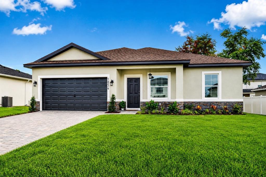 A single-story house with a black garage door, stone veneer base, and a paved driveway — 1854 SUPERIOR COURT, POINCIANA, FL
