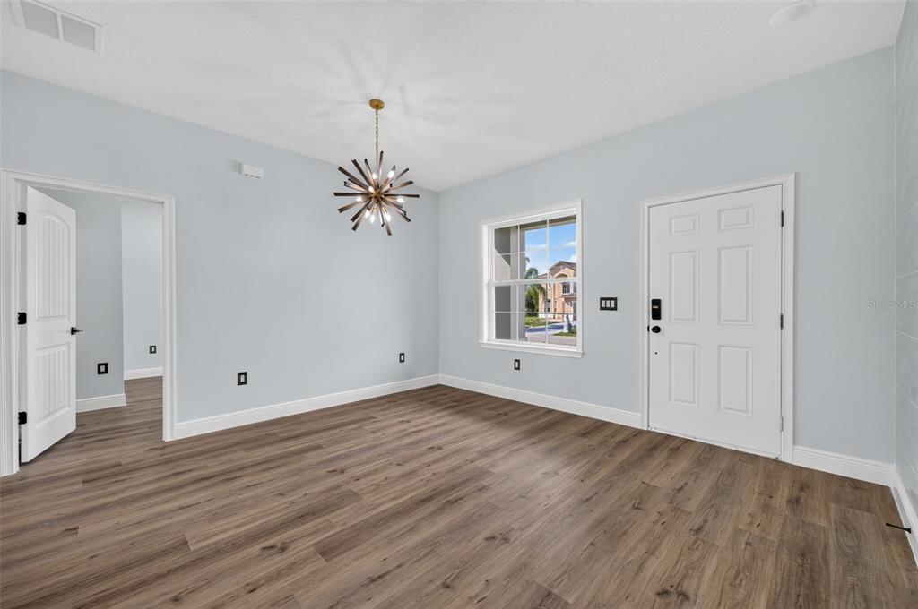 An empty room features light blue walls, wood-look flooring, a modern chandelier, and a white door — 1854 SUPERIOR COURT, POINCIANA, FL