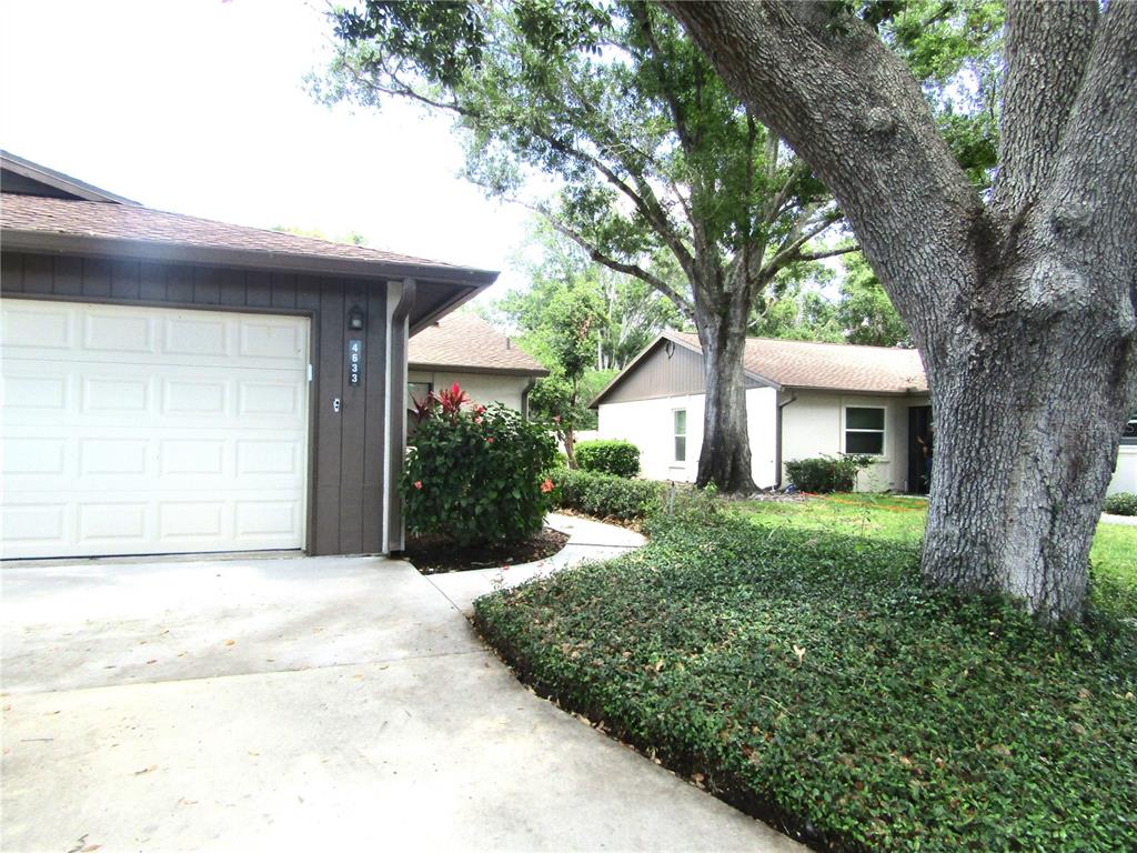 A single-story house with a white garage door, brown siding, and a large oak tree — 4633 OAK HILL DRIVE UNIT 13, SARASOTA, FL