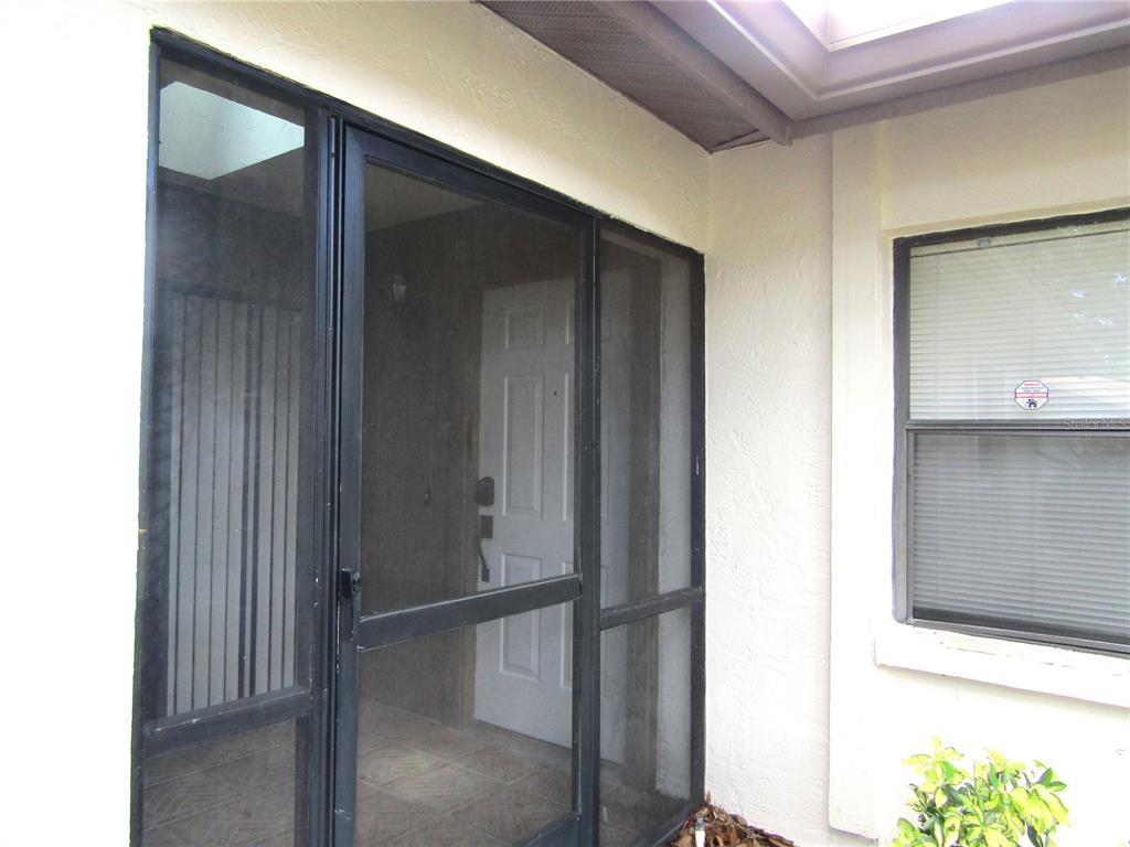 A white front door is visible behind a black metal screen door on a porch — 4633 OAK HILL DRIVE UNIT 13, SARASOTA, FL