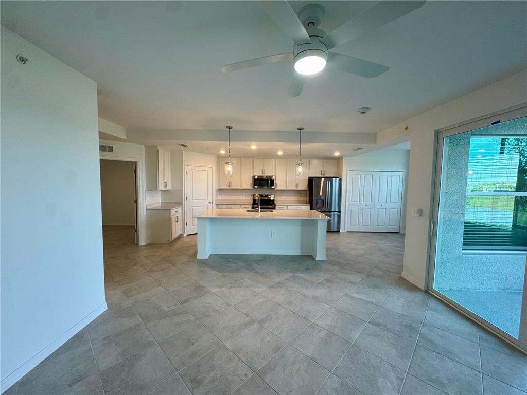 A kitchen with white cabinets, a central island, and tile flooring opens to a living area — 18923 SCALLOP LOOP UNIT 105, LAKEWOOD RANCH, FL