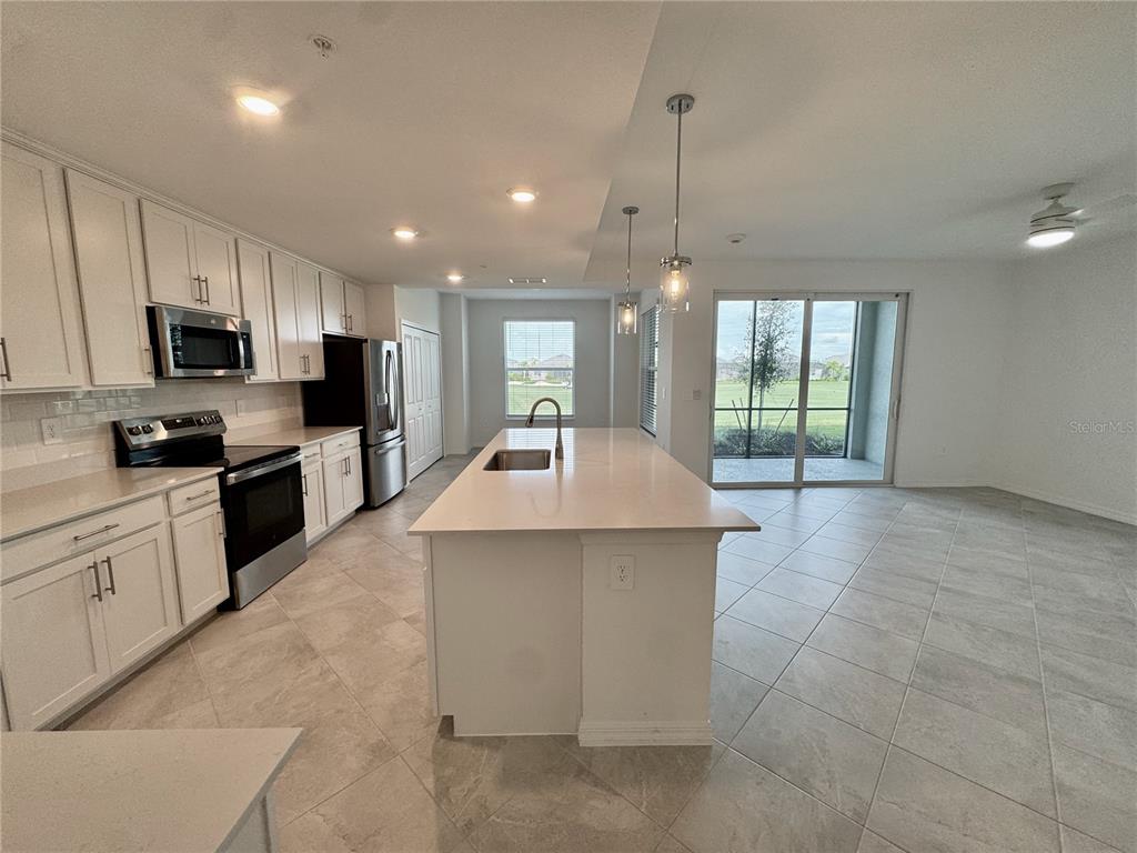 A modern kitchen features white cabinets, a large island, stainless steel appliances, and tile flooring — 18923 SCALLOP LOOP UNIT 105, LAKEWOOD RANCH, FL