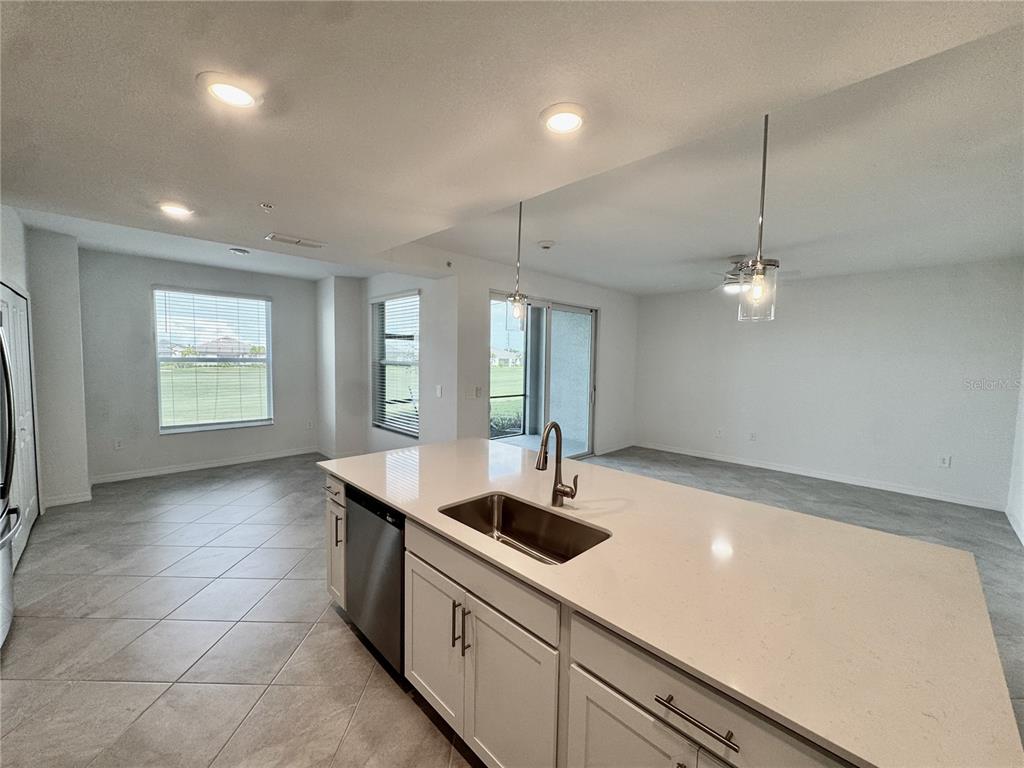 A kitchen island with a sink and white cabinets overlooks an open-concept living and dining area — 18923 SCALLOP LOOP UNIT 105, LAKEWOOD RANCH, FL
