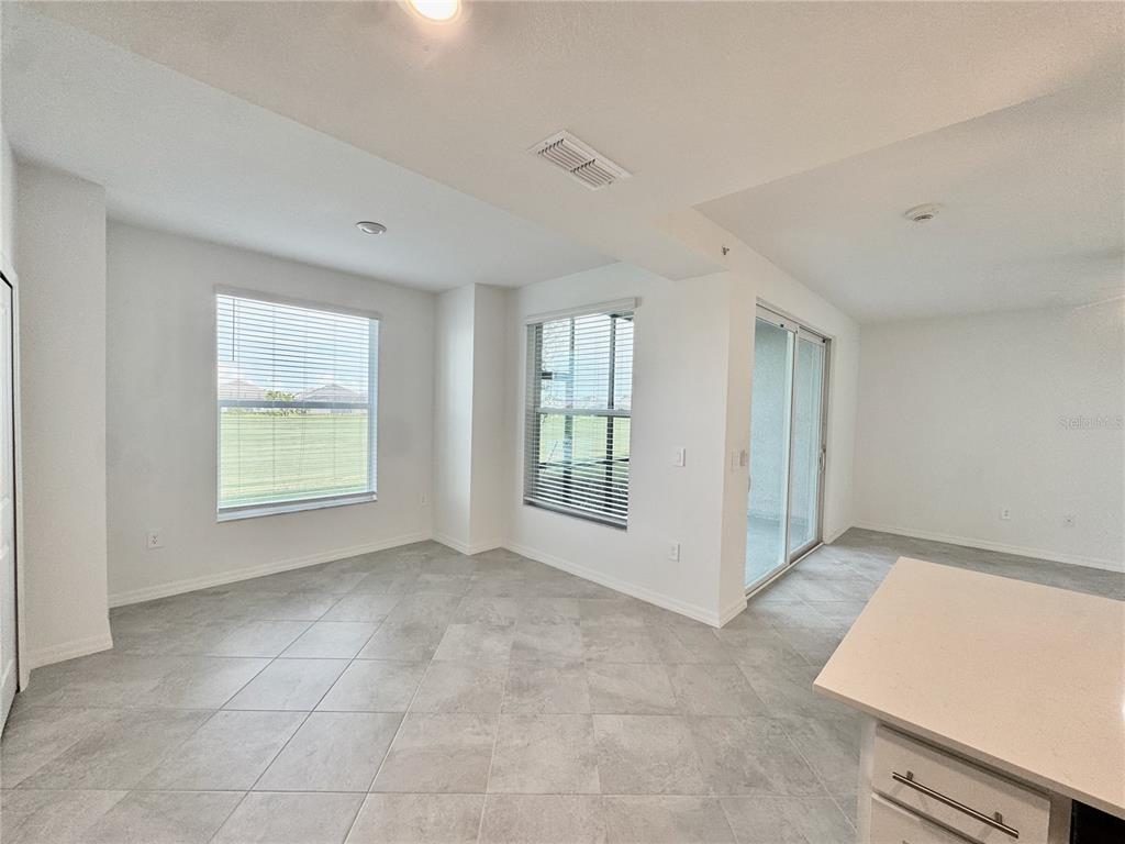 An open-concept dining area features light gray tile flooring, two windows, and a sliding door — 18923 SCALLOP LOOP UNIT 105, LAKEWOOD RANCH, FL