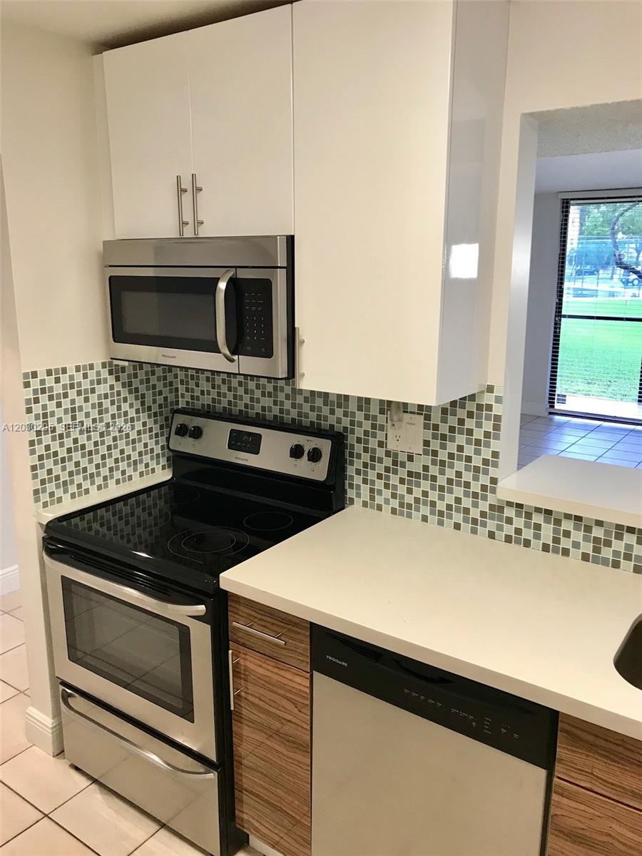 A kitchen features white upper cabinets, wood-grain lower cabinets, stainless steel appliances, and mosaic tile — 8015 SW 107th Ave # 120, Miami FL 33173, MIAMI, FL