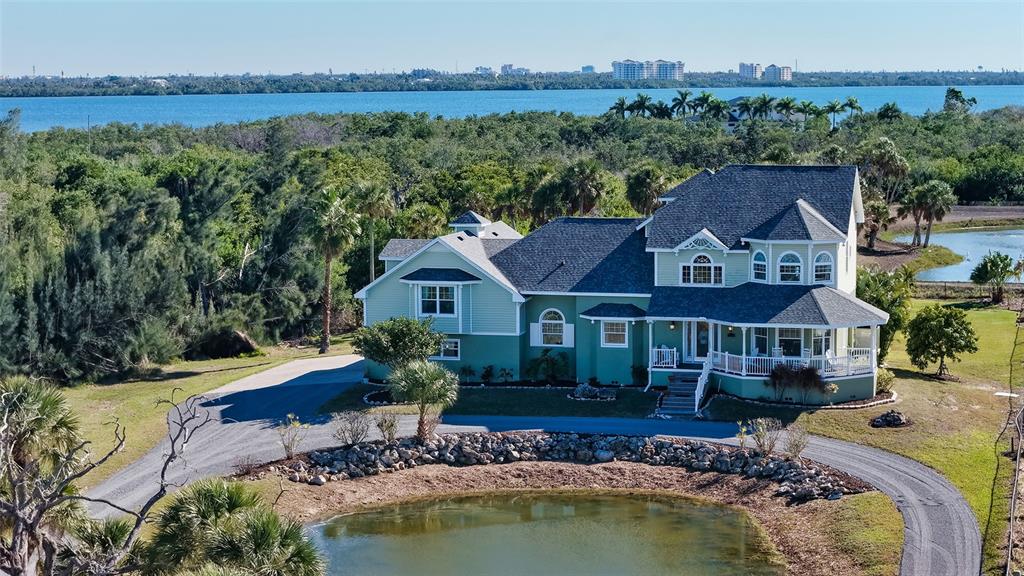An aerial view shows a two-story green house with a wraparound porch near a pond — 925 BAYSHORE DRIVE, TERRA CEIA, FL