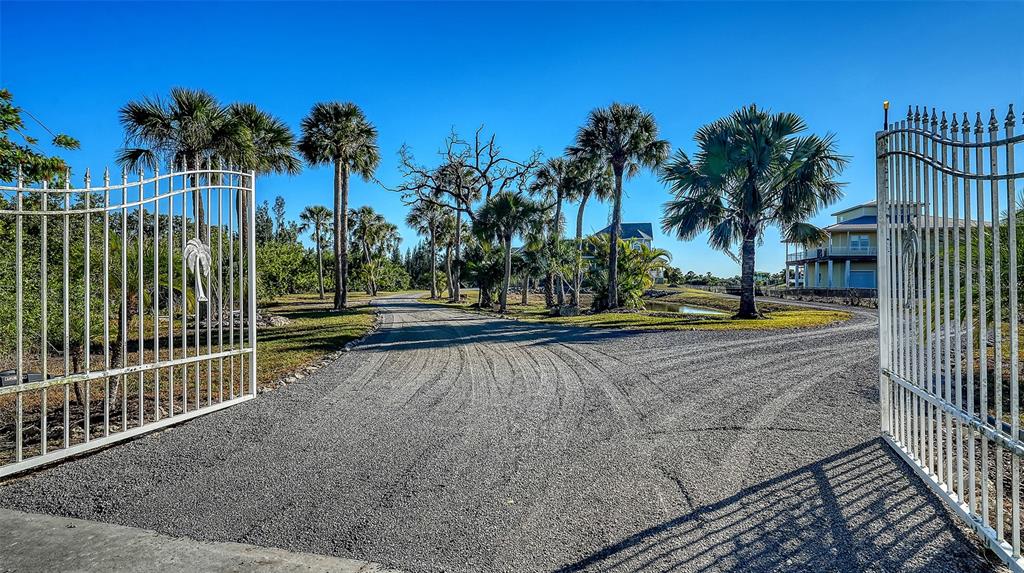 A gravel driveway leads through an open metal gate toward a house among palm trees — 925 BAYSHORE DRIVE, TERRA CEIA, FL