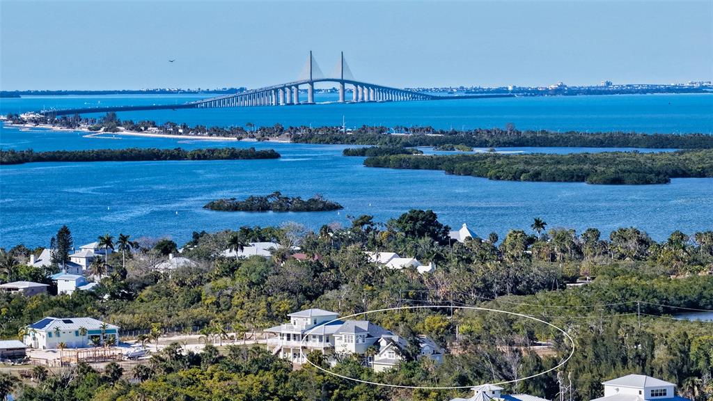 An aerial view shows a coastal house surrounded by dense trees near a large bridge — 925 BAYSHORE DRIVE, TERRA CEIA, FL