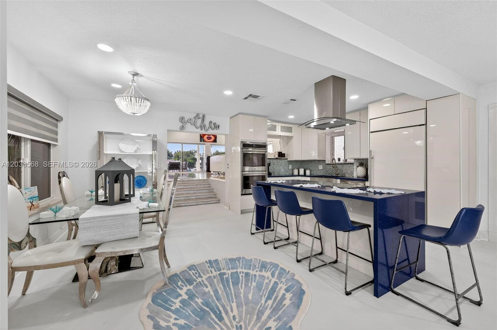 A modern kitchen and dining area feature a blue island, white cabinetry, and tile flooring — 317 S Riverside Dr, Pompano Beach FL 33062, POMPANO BEACH, FL