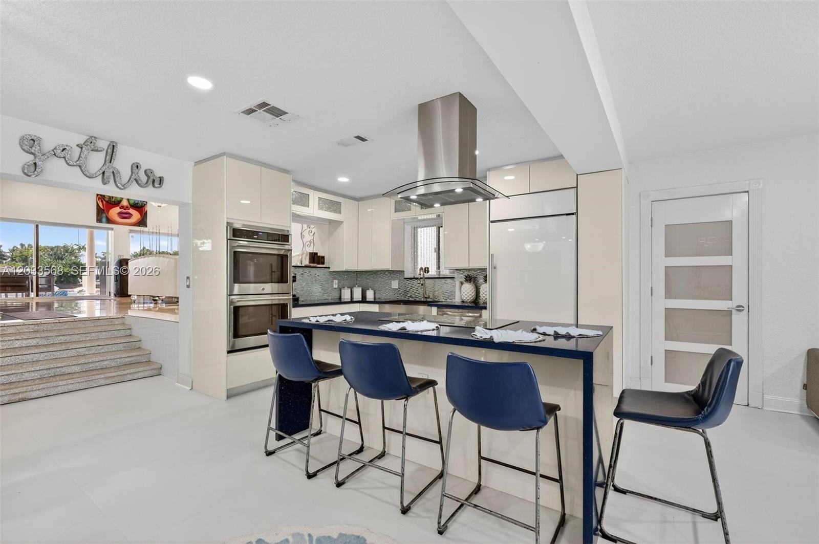 A modern kitchen features a blue island, stainless steel appliances, and glossy cream cabinetry — 317 S Riverside Dr, Pompano Beach FL 33062, POMPANO BEACH, FL