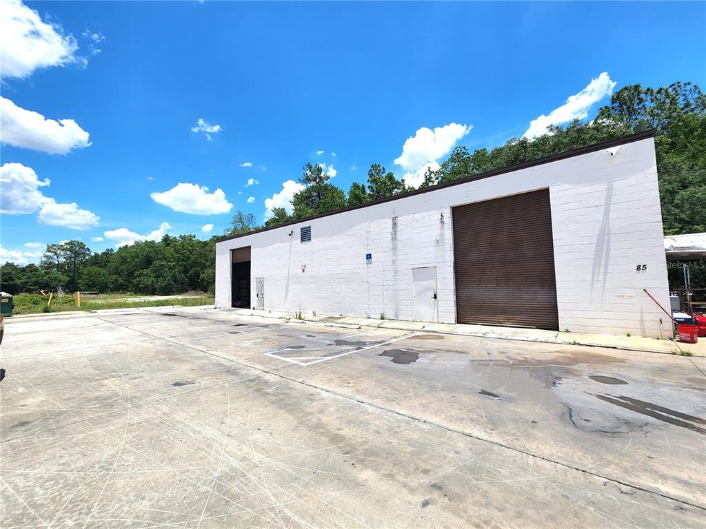A white concrete block warehouse building features two roll-up doors and a paved parking lot — 10857 SW 91 AVENUE UNIT C, OCALA, FL