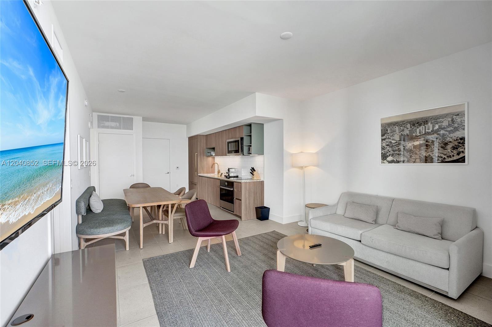 A modern living room features a kitchenette, dining area, and a large wall-mounted television — 159 NE 6th St # 3916, Miami FL 33132, MIAMI, FL